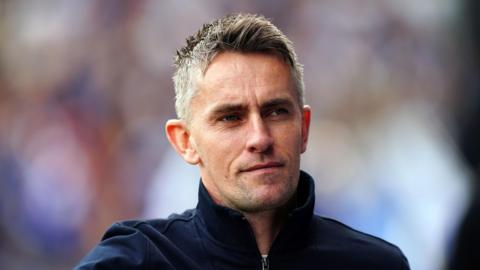 Keiran McKenna is in the middle of the image looking to the right. He has short grey hair and is wearing a navy quarter zip jacket.