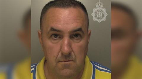 Police custody photograph of Matthew Full he has short black hair and is wearing a yellow shirt with blue and white stripes on the shoulders and collar 