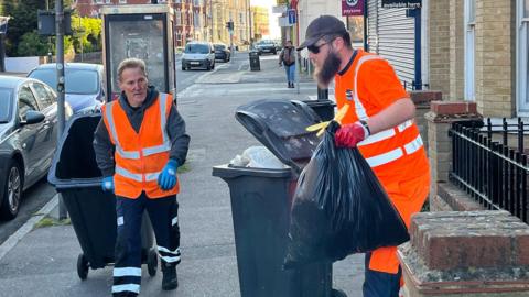 Two men in hi-vis orange vests collecting residential waste from homes in Canterbury Road, Margate.