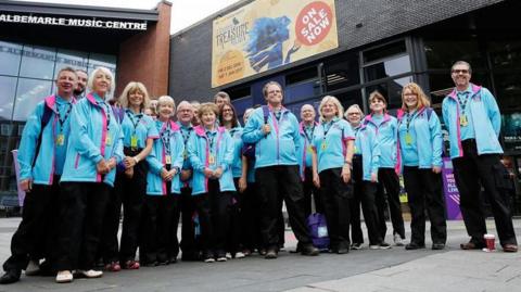 A group of about 30 volunteers, of all ages and both male and female, are standing outside Albemarle Music Centre in Hull city centre. They are all wearing sky blue coats that became synonymous with the 2017 City of Culture volunteers.