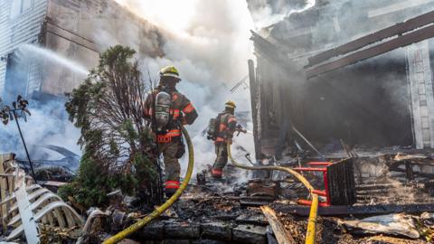 Firefighters carry hoses through the smoky remains of houses in an Oregon neighborhood