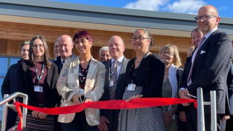 The ribbon cutting ceremony with dignitaries gathered behind a red ribbon with some shiny scissors being brandished