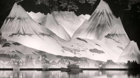 A black and white photo of an Alpine scene with peaks lit up behind small houses