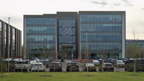 A four-storey office base with a 3 logo on its front in Green Park in Reading. Many cars are parked outside the offices.