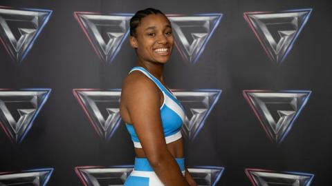 Emily Bell in a blue Gladiators kit, stands in front of the Gladiators branded wall