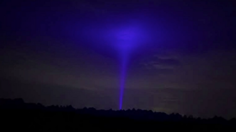 A bright blue hue in the dark sky, resembling a tornado-type shape, with a narrow stem and wider top. Dark trees can be seen in the foreground.