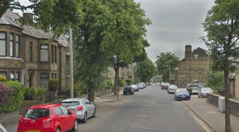 A residential street lined with trees and with cars parked on either side of the road