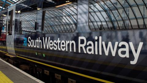 Side of dark blue train with white writing and edge of platform