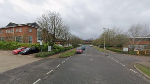A view of Harvest Crescent on a cloudy day. A few cars are parked by the business units.