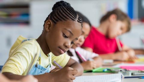 girl with cornrows writes in a school book