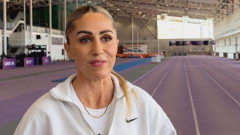 Ali Smith stood by an indoor athletics track in Loughborough, wearing a white top. 