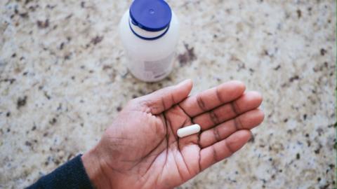 A supplement in a hand with a bottle in the background