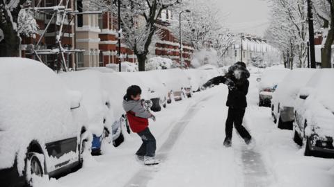 Two children having a snowball fight in a snow-covered suburban street