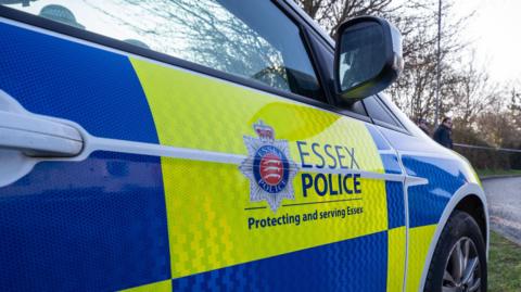 Stock photo showing the side of an Essex Police car which has been parked on a patch of grass