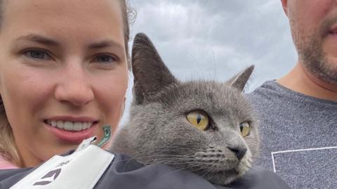 A woman holds a grey British shorthair cat.