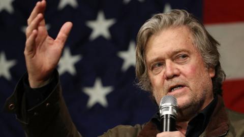 photo of Steve Bannon speakin into a microphone in front of an American flag