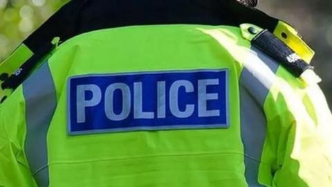 A close up picture of the back of a police officer showing his bright yellow police jacket. 