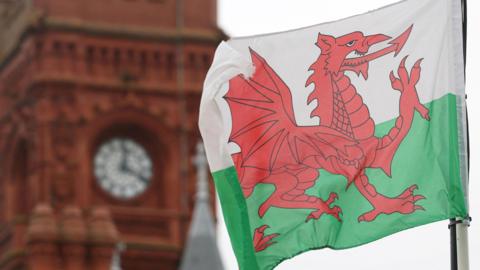 Baner Cymru yn chwifio o flaen adeilad Y Pierhead ym Mae Caerdydd