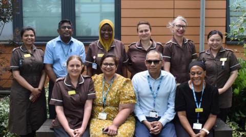 Two rows of staff members - one row is standing and one row is sitting, with Poonam sitting in the middle, wearing a yellow dress.
