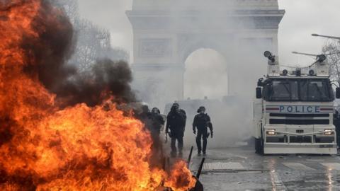 French riot police forces stand behind a burning barricade on the Champs-Elysees in Paris on March 16, 2019, during the 18th consecutive Saturday of demonstrations called by the "Yellow Vest" (gilets jaunes) movement.