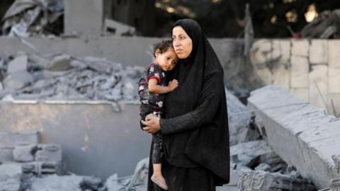 A Palestinian woman looks on holding a child at the site surrounding an evacuated UNRWA clinic where displaced people were taking shelter, following an overnight Israeli strike, in Gaza City August 6, 2025.