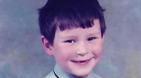 A young boy with black hair smiles at the camera