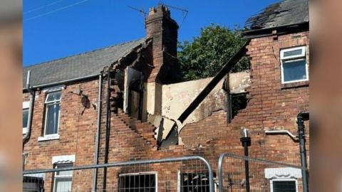 The house, with its roof ripped off and windows smashed