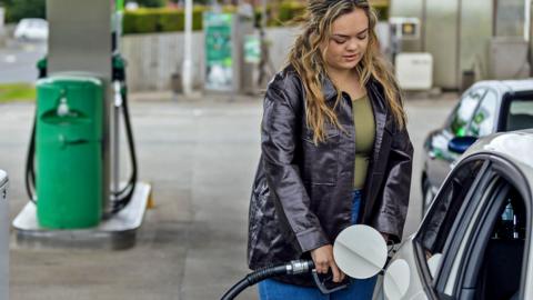 A woman fills her car up at a petrol station