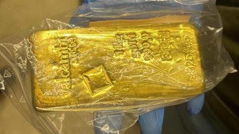 A solid gold block with engravings saying '1kg gold, 999,9' inside a clear plastic bag