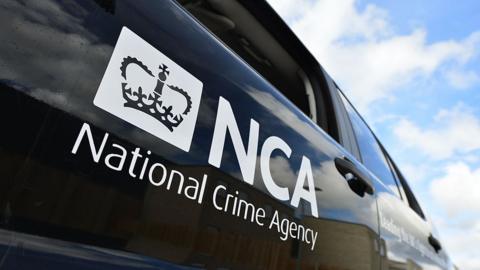 The side of a black National Crime Agency vehicle showing the agency's logo on the door