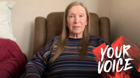 A woman with long, light brown/blonde hair in a striped jumper sitting on a brown leather chair