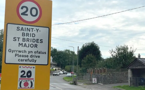 Arwydd melyn yn nodi enw Saint-y-brid wrth ymyl heol yn y pentref. Mae'r arwydd hefyd yn nodi terfyn cyflymder o 20 milltir yr awr.