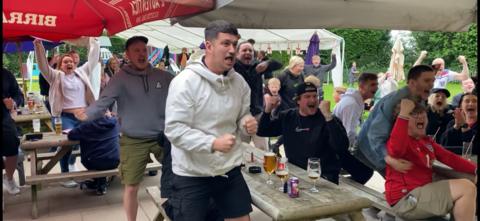 Fans in a beer garden cheering and punching the air in excitement