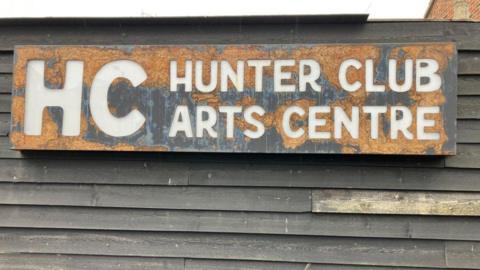 A large sign on a wall made up of wooden panels which reads HC Hunter Club Arts Centre