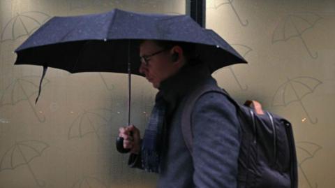 a man holds a black umbrella above his head as he walks along a street