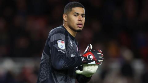 Seny Dieng holding the ball in a dark Middlesbrough goalkeeping jersey during a game