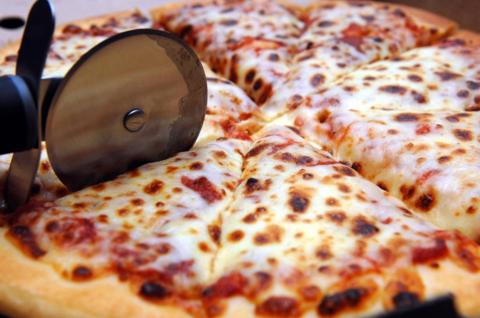 A round metal pizza cutter being used to cut a cheese and tomato pizza