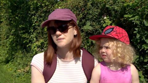 A woman and her daughter are interviewed while sitting next to a hedge.