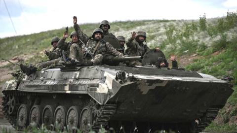 Ukrainian servicemen wave as they move towards a checkpoint near the city of Lysychansk in the eastern region of Donbas on 23 May