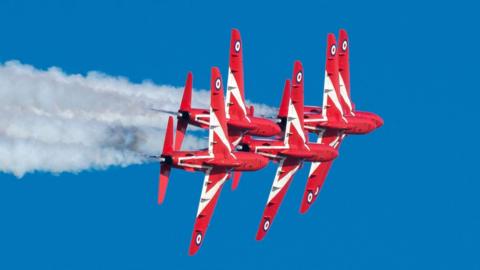 Five bright red jet planes fly together in a tight formation. 