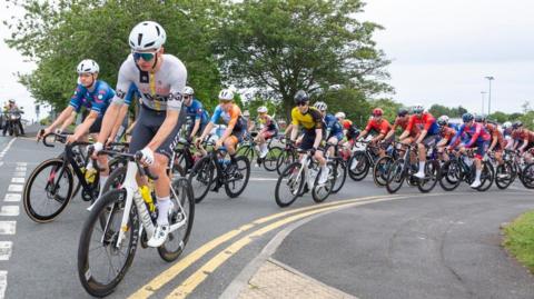 Dozens of male cyclists in helmets and cycling gear turning at a junction during Consett Cycle Festival on 22 June 2025.