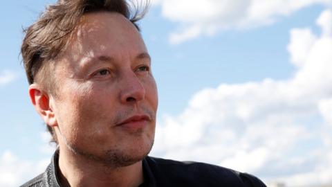 Elon Musk looks into the middle distance in a close-up against a blue sky