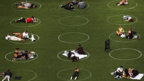 An aerial view showing people relaxing in a park whilst staying designated white circles to ensure social distancing