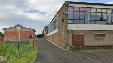 An old school building in the Borders with many windows and brick walls and tarmac around it