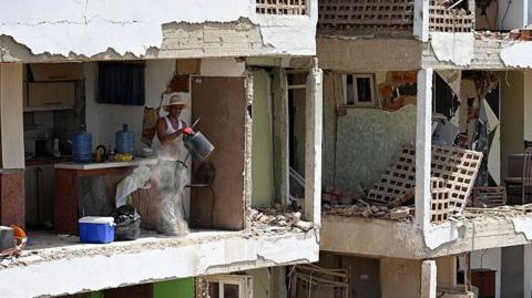 A man removes debris using a bucket inside a heavily damaged apartment
