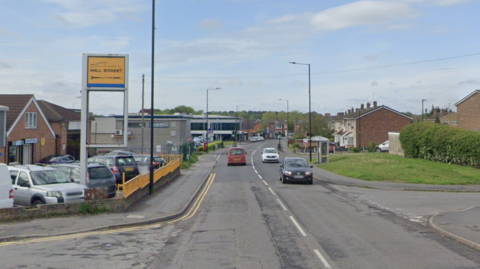 General view of Mill Street in Armthorpe, with a garage on the left-hand side, houses on the right and cars driving along the road.