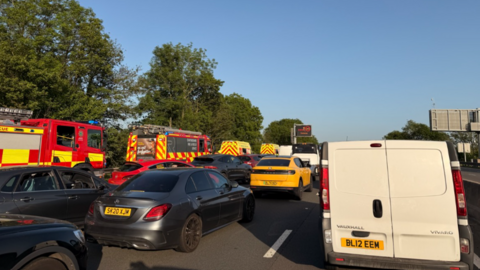 A queue of cars and vans on a motorway with a number of fire engines on the left hand side