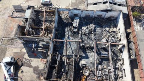 An aerial view of a burnt out building with wrecked cars inside