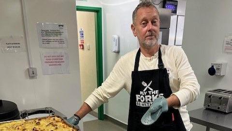 A man wearing a chef's apron stands over a tray of food he has made at the Julian Trust in Bristol