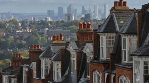 On the right, red-brick houses in a street in the suburban district of Muswell Hill while in the background is the skyline of City of London